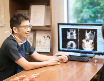 モニターのレントゲン画像を前に説明する歯科医師