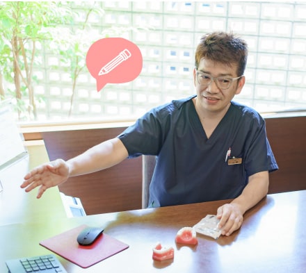 診療室のデスクで説明する歯科医師
