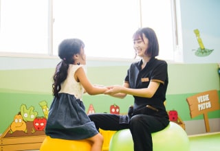 バランスボールに座り女の子と手をつなぐスタッフ